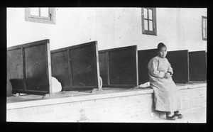 Woman sitting near a bank of toilets, China, ca. 1920-1940