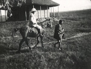 Missionary on horseback preceded by an African