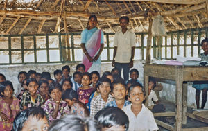 16.- Mission for børn i Indien. Diasserie 1990, "Da jeg blev velsignet af en elefant". Inde i skolen sidder en masse elever i ét stort rum. Og så er der f.eks. 3 klasser uden vægge imellem. De sidder bare på gulvet – den ene klasse er måske ved at lære et alfabet, den anden er ved at synge en sang, og den tredje skal lære matematik – ét stort rod!