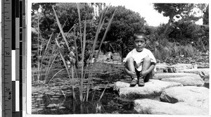 Serious faced Japanese boy sitting on a rock in Maryknoll mission garden near Lake Biwa, Japan, ca. 1947