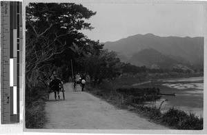 Two women travel by rickshaw on a road next to the Kuma River, Yatsushiro, Japan, ca. 1908