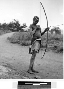 Boy standing on a dirt road holding a bow and arrow, Africa, 1950