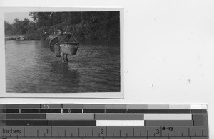 A boy carries large baskets through the water at Dongan, China, 1940