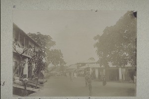 A street in Kumase, to the left a German trading store. There where the streetlamp is standing used to be the place of executions