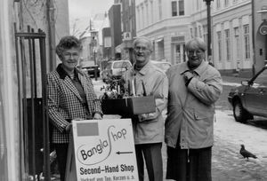 Bangla-Shoppen i Flensborg blev startet af den lokale Dansk Santalmission-afdeling i 1984 - af Hedi og Walter Lorenzen, som efter en rejse til Saraswatipur Kostskole var optaget af at støtte uddannelse af skolebørn i Bangladesh. Dette sker bl.a. ved formidling af fadderskaber til fattige børn. (Fra højre: Hedi Lorenzen, Walter Lorenzen, (NN)). I dag deler initiativgruppen Bangla -Shoppen med Flensborgs Y's Men's Club, som dermed også støtter arbejdet, der i 2014 fejrede 30 års jubilæum