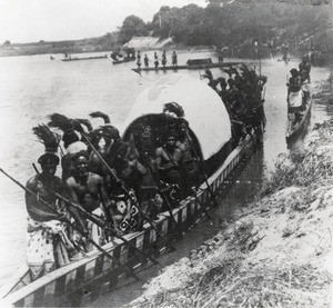 The Nalikwanda (royal barge) approaching the river bank ; paddlers in the foreground