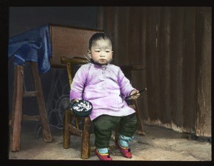 Toddler sitting in a chair holding chopsticks and a bowl of rice, China, ca.1917-1923