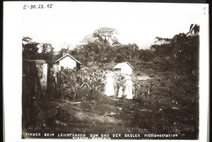 Children carrying clay to build the Mission Station Nyasoso (Cameroon). Mrs Basedow, Mrs Walker and child