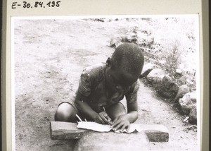 A schoolgirl from Itoki. She is using the rib of a palm leaf to write on a banana leaf