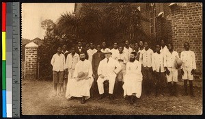 Missionary fathers and others sit before a school building, Congo, ca.1920-1940