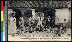 Orphans sitting among missionary sisters and eating a meal, India, ca.1920-1940