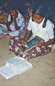 07.- Mission for børn i Indien. Diasserie 1990, "Da jeg blev velsignet af en elefant". Her sidder Bejnemal og laver lektier. Det gør hun udenfor om aftenen. Hun sidder og skriver på en tavle, og hun sidder på jorden