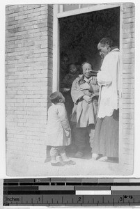 European clergyman standing in a doorway with women and children, China, ca. 1919