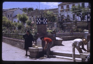 woman, boy and man filling containers with water at city fountain