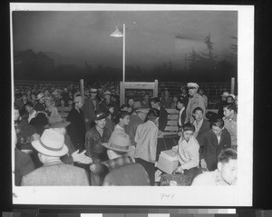 "Part of a 10-day evacuation program, Japanese at the Santa Anita assembly center are shown in the process of departing. At dawn, evacuees crowd gate to check baggage, all labeled for shipment on the train with them."--caption on photograph