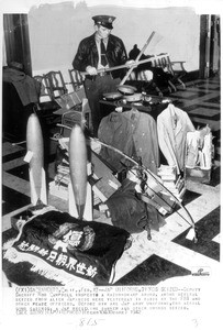 "Deputy Sheriff Rod Campbell of Sacramento inspects a razor sharp sword among several seized from Japanese there. Before him are Jap army uniforms, two aerial bomb casings, a wrestlying banner and other articles taken by the FBI."--caption on photograph