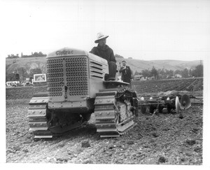 "G. Nagano (Nisei) cultivating truck garden with tractor at Gardena. The most modern equipment is used on this farm."--caption on photograph