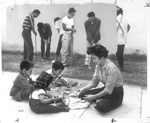 "Help Here--some of the flock of young people who regularly gather at her Long Beach home-recreational center practice golf swings behind Mrs. Sue Joe. She plays with David Ater and her Rand, 3, Lisa, 1."--caption on photograph