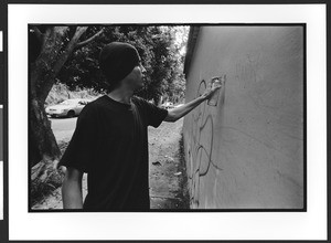 A young man spray paints, "tags",on a wall, San Salvador