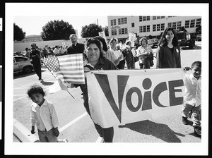 Woman and child carrying banner at head of procession while waving an American flag, Industrial Areas Foundation, Los Angeles, 1996