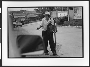 A beggar of Hispanic origin standing along the side of a road with his hand out, San Salvador