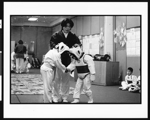 Two boys shake hands before martial arts fight with instructor watching, Oriental (Los Angeles), 1996