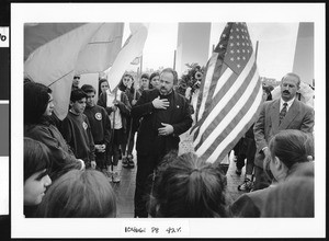 Priest speaking to group next to an American Flag, Los Angeles, 1999