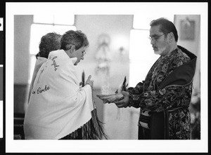 Priest offering religious article to two women, Los Angeles, 1999