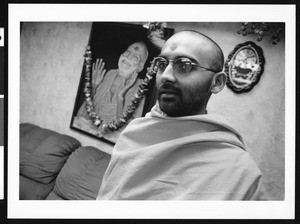 Man in robes stands in front of a smiling picture, Los Angeles, 1999