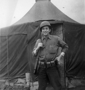 Martin J. Bolhower with rifle, in front of tent