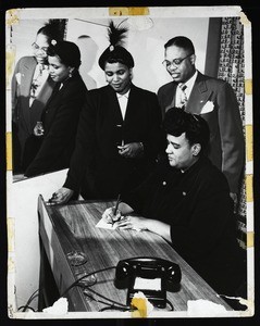 Unidentified woman signing at a desk as an unidentified couple look on, COGIC