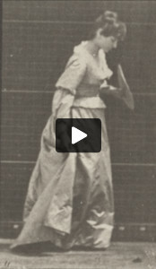 Woman in long dress stooping and lifting dress with a fan in left hand