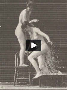 Nude woman pouring a bucket of water over another nude woman