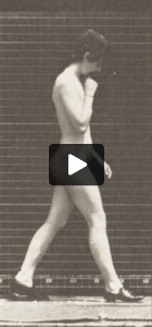 Nude woman walking with shoes on and right hand at chin