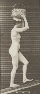 Nude woman ascending an incline with a 20-lb. basket on head