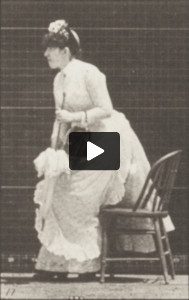 Woman in long dress with parasol in left hand placing a chair and sitting