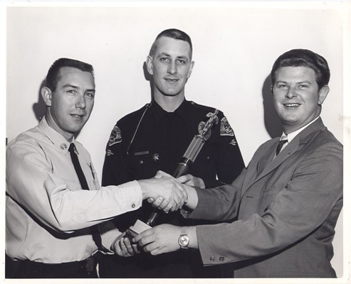 Two Policemen and a Civilian Shaking Hands Over a Trophy