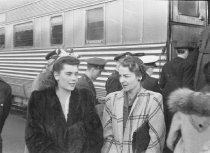 Two women outside passenger train with others in background, saying good-bye, unknown