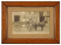 Framed sepia photograph depicts a man standing in front of a large wagon