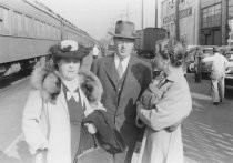 Two women and one man standing outside in front of passenger train, unknown