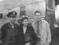 Military man, woman and man standing outside passenter train, unknown