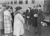 Several people standing in front of a passenger train saying good bye to military man and his wife, unknown