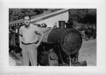 Man standing in front of a locomotive with a shed type building in background, unknown