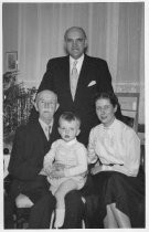 Three adults with child sitting on what appears to be grandfather's lap at Christmas, unknown