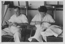 Man and woman sitting in what look like deck chairs on a ship, unknown