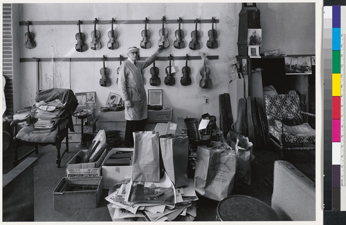 [Man standing next to wall of violins.]