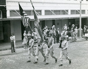 Photograph of Gammey Bearing A Military Flag While Marching Down the Street in England