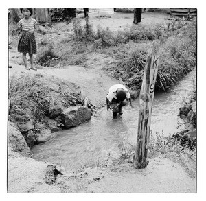 Boy wearing boots steps crouches down into a stream, Korea