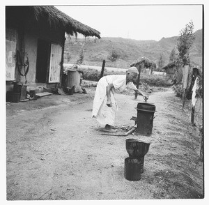 Stooped elderly woman cooks on outside stove, Korea