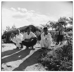Three men squatting, one man standing outside a thatched roof house, South Korea